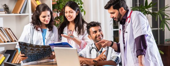 Successful Young Indian asian medical doctors are using a laptop and smiling while having a discussion at table